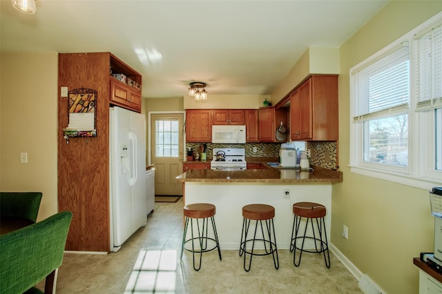 kitchen with a kitchen breakfast bar, backsplash, white appliances, and kitchen peninsula