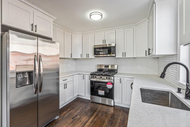 kitchen with appliances with stainless steel finishes, sink, white cabinets, dark hardwood / wood-style flooring, and light stone counters