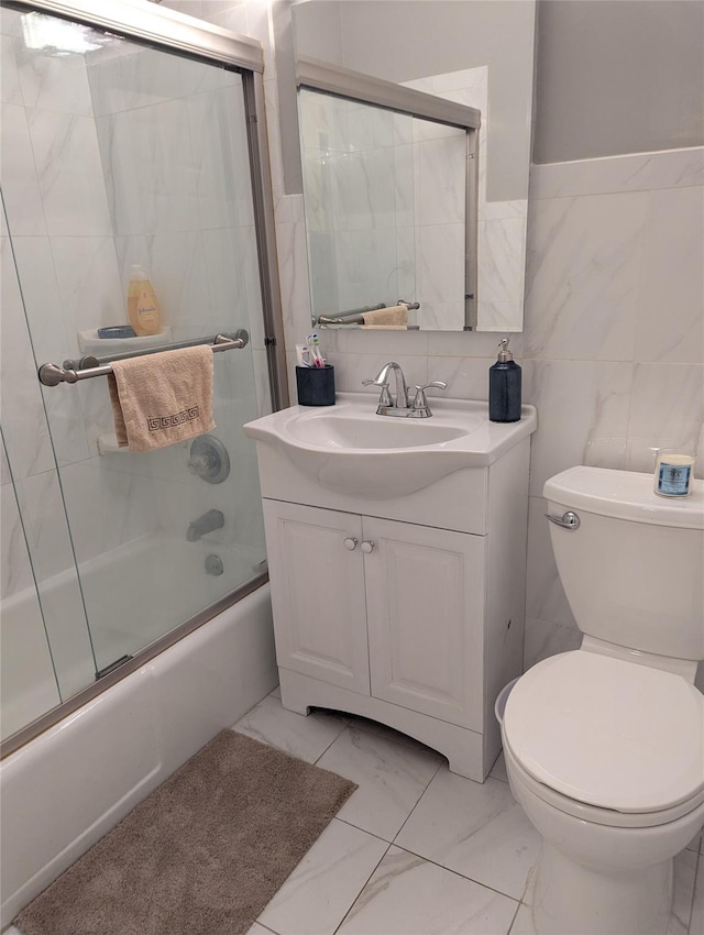 full bathroom featuring vanity, bath / shower combo with glass door, tile walls, and toilet