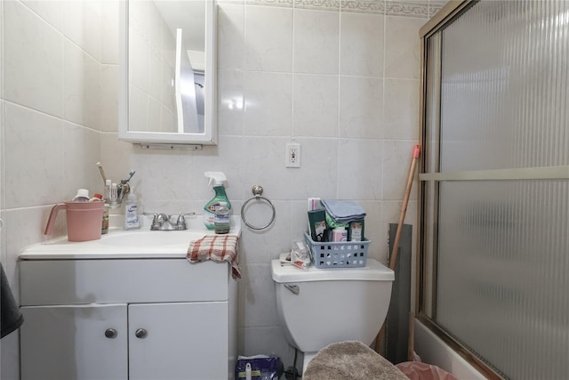 full bath featuring combined bath / shower with glass door, toilet, tile walls, and vanity