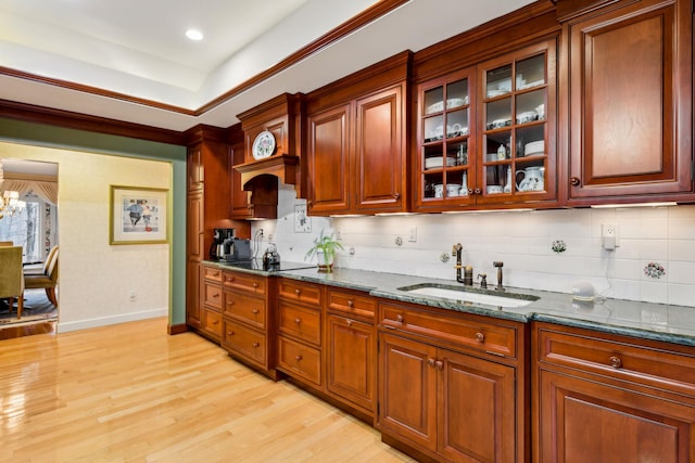 kitchen featuring sink, dark stone countertops, backsplash, black electric stovetop, and light hardwood / wood-style floors