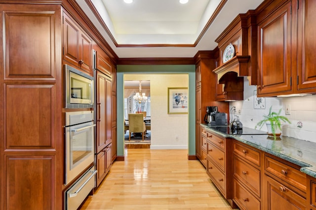 kitchen featuring appliances with stainless steel finishes, backsplash, a chandelier, dark stone counters, and light wood-type flooring