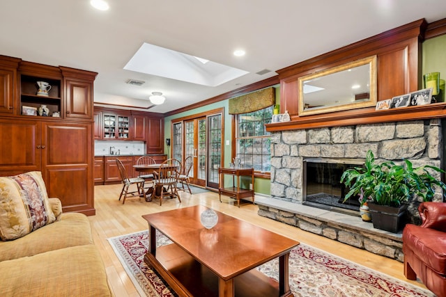 living room with sink, a skylight, a fireplace, ornamental molding, and light hardwood / wood-style floors