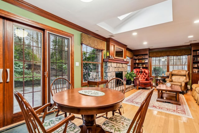 dining area with hardwood / wood-style floors, a stone fireplace, a skylight, and ornamental molding