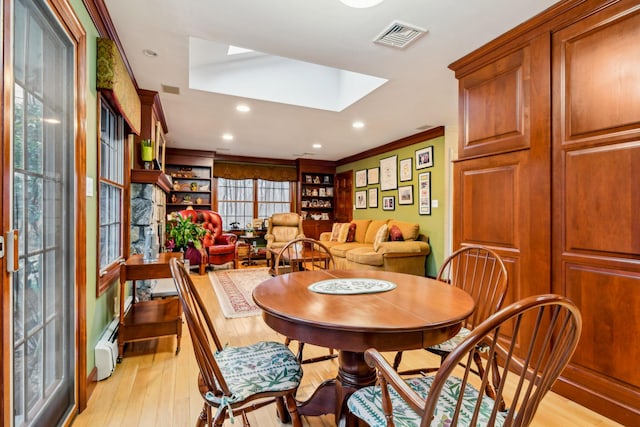 dining room with a baseboard radiator, ornamental molding, light hardwood / wood-style flooring, and a skylight