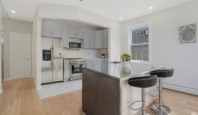 kitchen with light hardwood / wood-style flooring, gray cabinets, appliances with stainless steel finishes, a kitchen breakfast bar, and kitchen peninsula