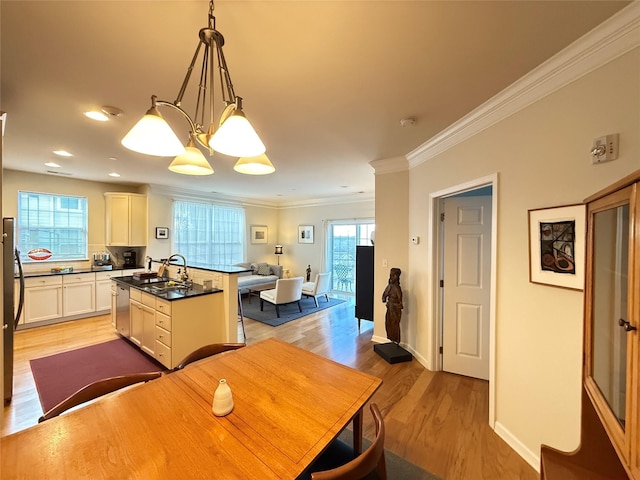 kitchen featuring crown molding, light wood-type flooring, stainless steel dishwasher, pendant lighting, and a kitchen island with sink