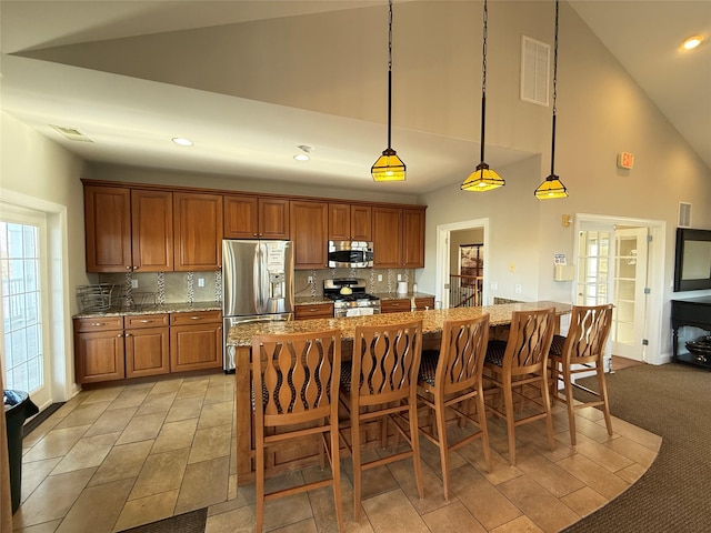 kitchen featuring a kitchen bar, hanging light fixtures, appliances with stainless steel finishes, light stone countertops, and decorative backsplash