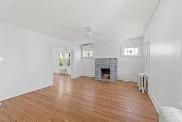 unfurnished living room featuring a wall unit AC, radiator heating unit, a brick fireplace, and light wood-type flooring