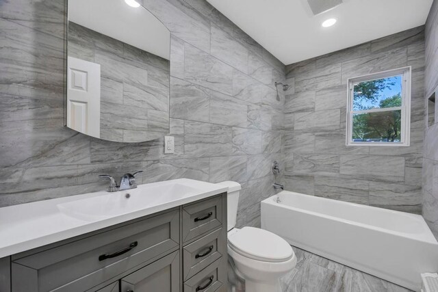 full bathroom with vanity, tile walls, toilet, and shower / bath combination