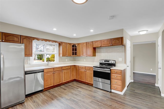 kitchen featuring appliances with stainless steel finishes, sink, backsplash, and light wood-type flooring