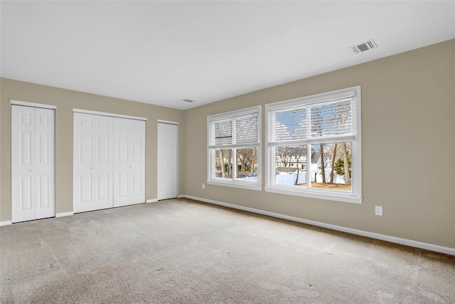 unfurnished bedroom featuring multiple closets and light carpet