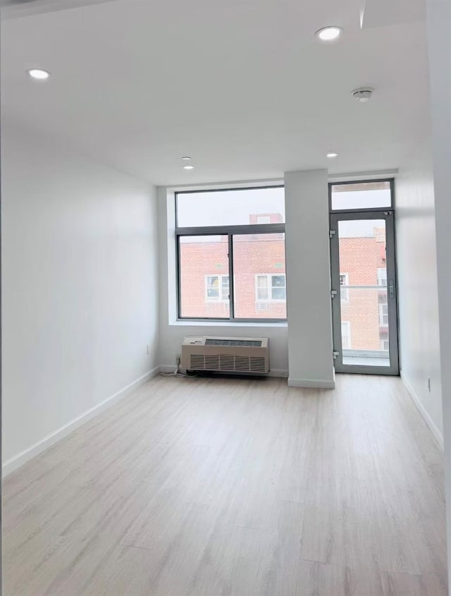 unfurnished room with a wealth of natural light, a wall unit AC, and light hardwood / wood-style floors