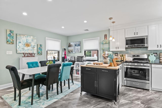 kitchen featuring stainless steel appliances, white cabinetry, pendant lighting, and backsplash