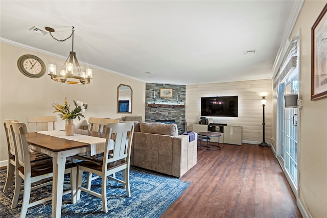 dining area with dark hardwood / wood-style flooring, a stone fireplace, ornamental molding, and an inviting chandelier