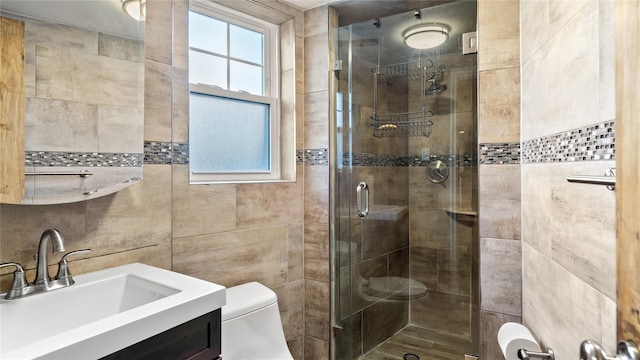 bathroom with a shower with door, vanity, tile walls, and toilet