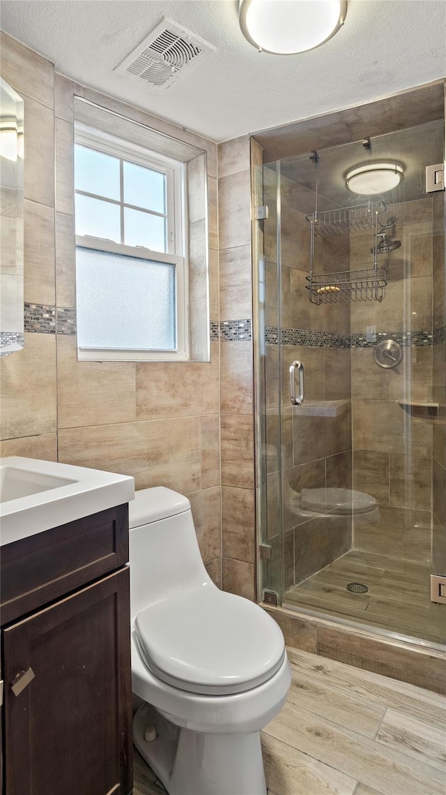 bathroom featuring tile walls, vanity, a textured ceiling, toilet, and walk in shower