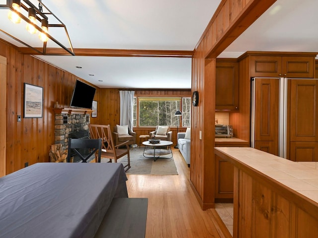 bedroom featuring paneled refrigerator, a fireplace, light wood-type flooring, and wood walls