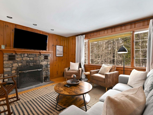 living room with hardwood / wood-style flooring, wooden walls, a stone fireplace, and a wealth of natural light