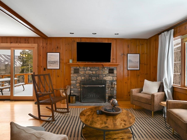 living room featuring a fireplace, light wood-type flooring, beam ceiling, and wood walls