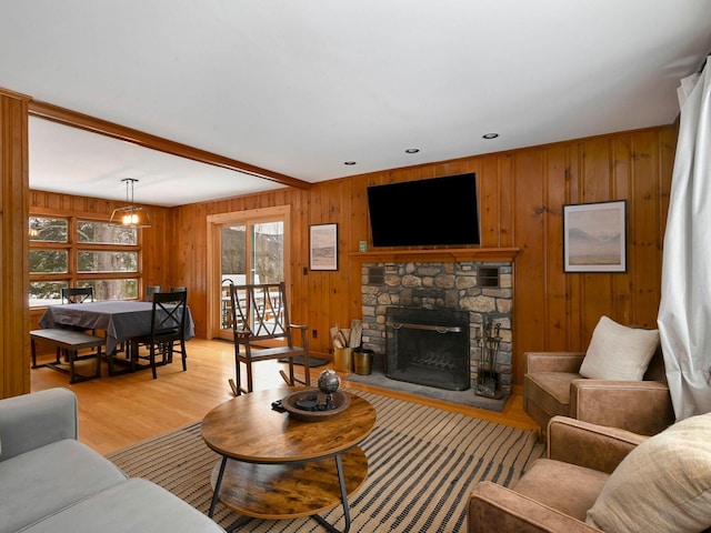 living room featuring wooden walls, a stone fireplace, beam ceiling, and light hardwood / wood-style flooring