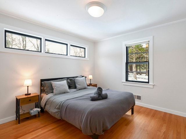 bedroom with multiple windows, crown molding, and light hardwood / wood-style flooring