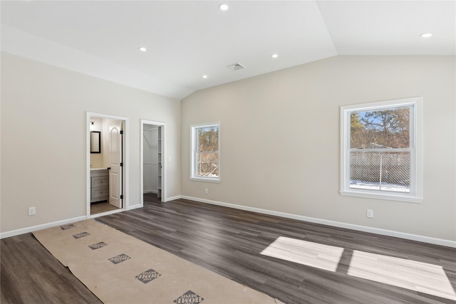 unfurnished bedroom featuring vaulted ceiling, dark hardwood / wood-style floors, ensuite bath, and a spacious closet