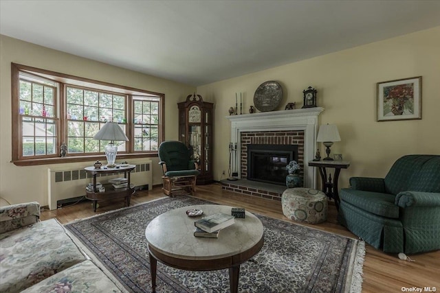 living room with a brick fireplace, radiator heating unit, and wood-type flooring