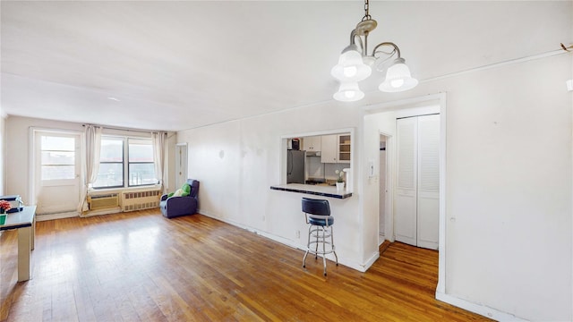 kitchen with a breakfast bar area, white cabinetry, wood-type flooring, stainless steel refrigerator, and pendant lighting