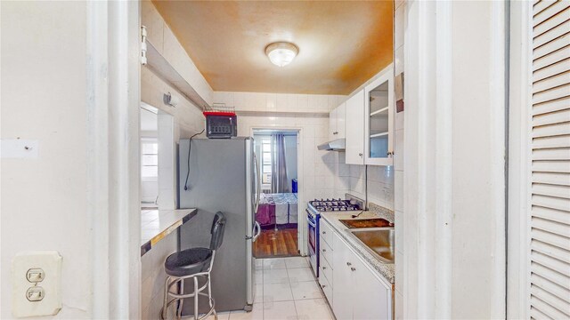 kitchen featuring sink, appliances with stainless steel finishes, white cabinets, light tile patterned flooring, and decorative backsplash