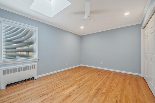 unfurnished room featuring crown molding, a skylight, light wood-type flooring, radiator, and ceiling fan