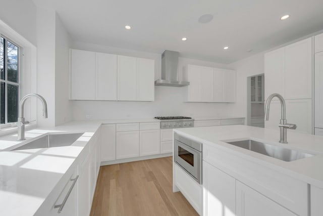 kitchen with sink, stainless steel appliances, white cabinets, and wall chimney exhaust hood