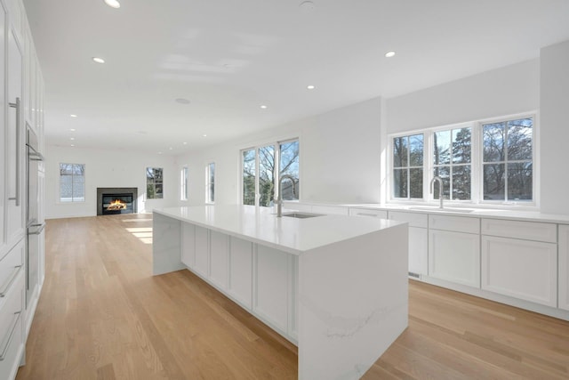 kitchen with a kitchen island with sink, sink, light hardwood / wood-style floors, and white cabinets