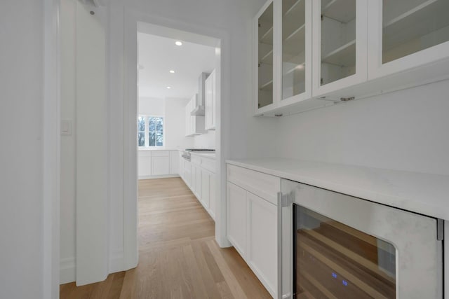 bar with white cabinetry, wall chimney exhaust hood, beverage cooler, and light hardwood / wood-style flooring