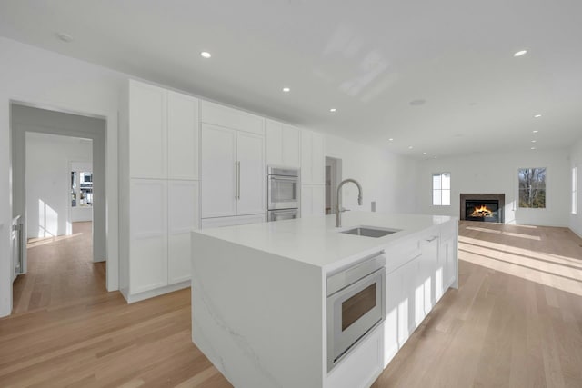 kitchen featuring built in microwave, sink, an island with sink, and white cabinets