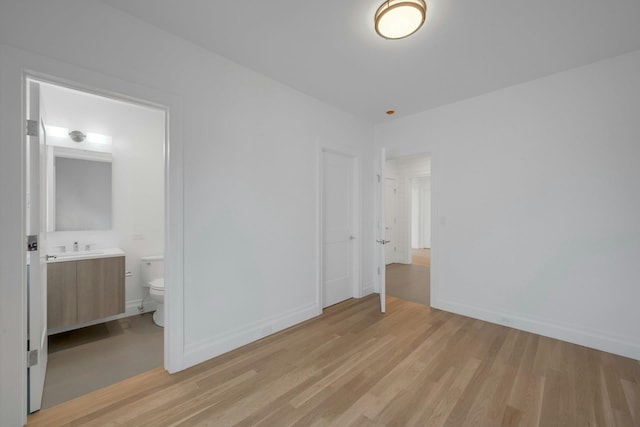 unfurnished bedroom featuring ensuite bathroom, sink, and light hardwood / wood-style floors