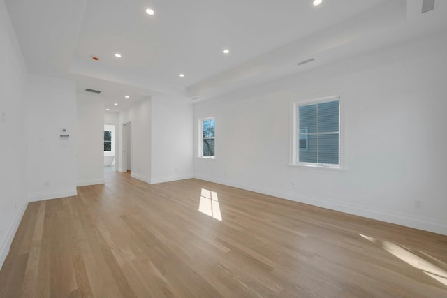 empty room featuring light wood-type flooring and a tray ceiling