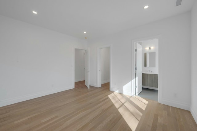 unfurnished bedroom featuring a spacious closet, ensuite bath, and light wood-type flooring