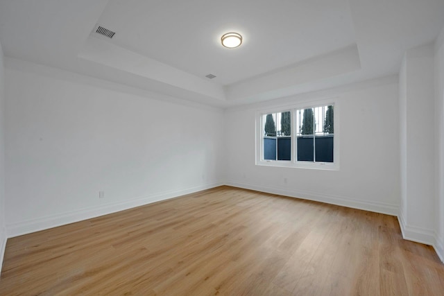 empty room with a raised ceiling and light wood-type flooring