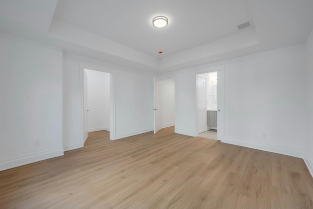 empty room with a raised ceiling and light wood-type flooring