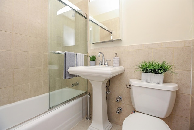 bathroom featuring tile walls, bath / shower combo with glass door, tile patterned floors, and toilet