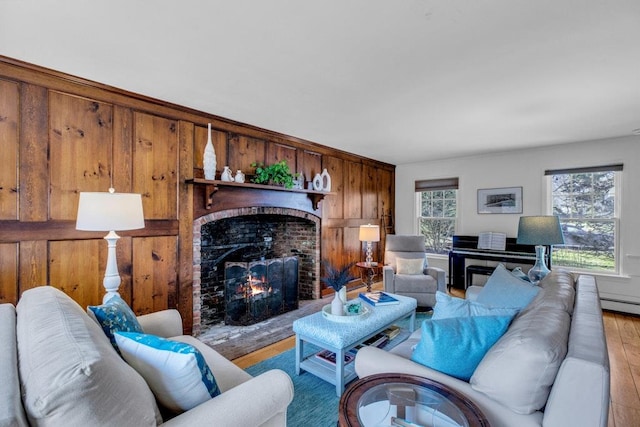 living room with baseboard heating, a brick fireplace, and light hardwood / wood-style flooring