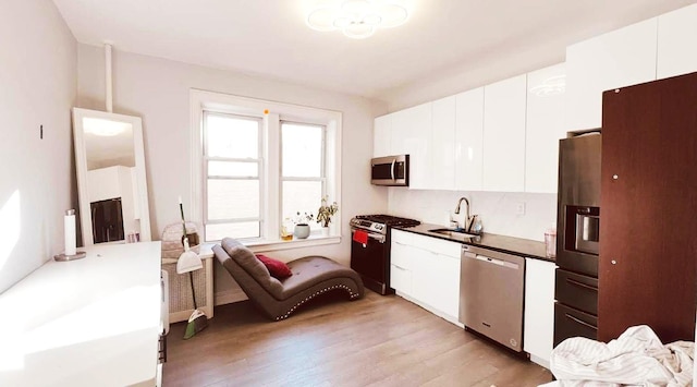 kitchen with appliances with stainless steel finishes, sink, white cabinets, and light wood-type flooring