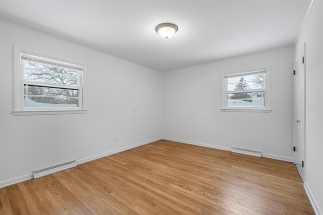 spare room featuring a baseboard heating unit, crown molding, light hardwood / wood-style flooring, and a healthy amount of sunlight