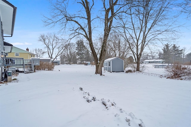 yard covered in snow with a wooden deck and a storage unit