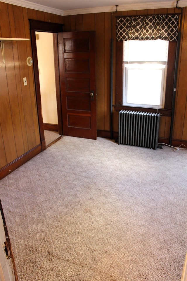 carpeted empty room featuring ornamental molding, radiator heating unit, and wood walls