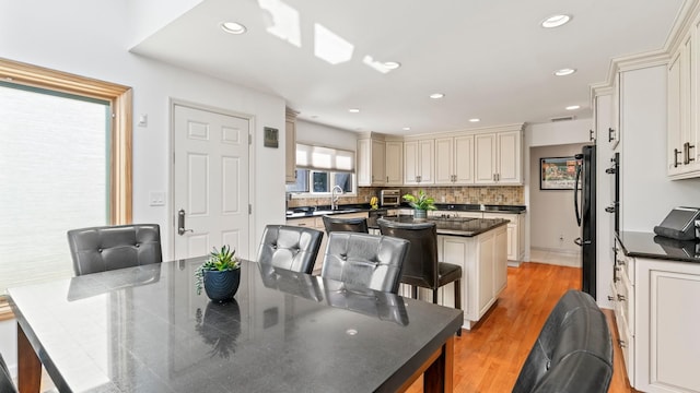 kitchen featuring sink, backsplash, a kitchen island, a kitchen bar, and light wood-type flooring