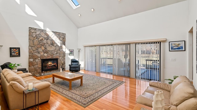 living room featuring high vaulted ceiling, a fireplace, a skylight, and hardwood / wood-style floors