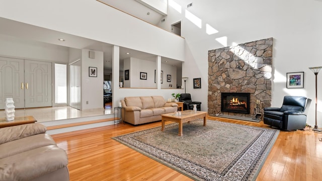 living room with a high ceiling, wood-type flooring, and a stone fireplace