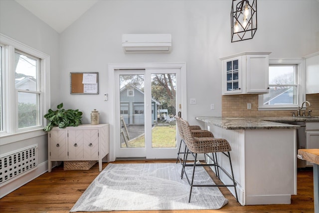 kitchen featuring a kitchen breakfast bar, dark hardwood / wood-style floors, a wall mounted AC, white cabinets, and decorative light fixtures